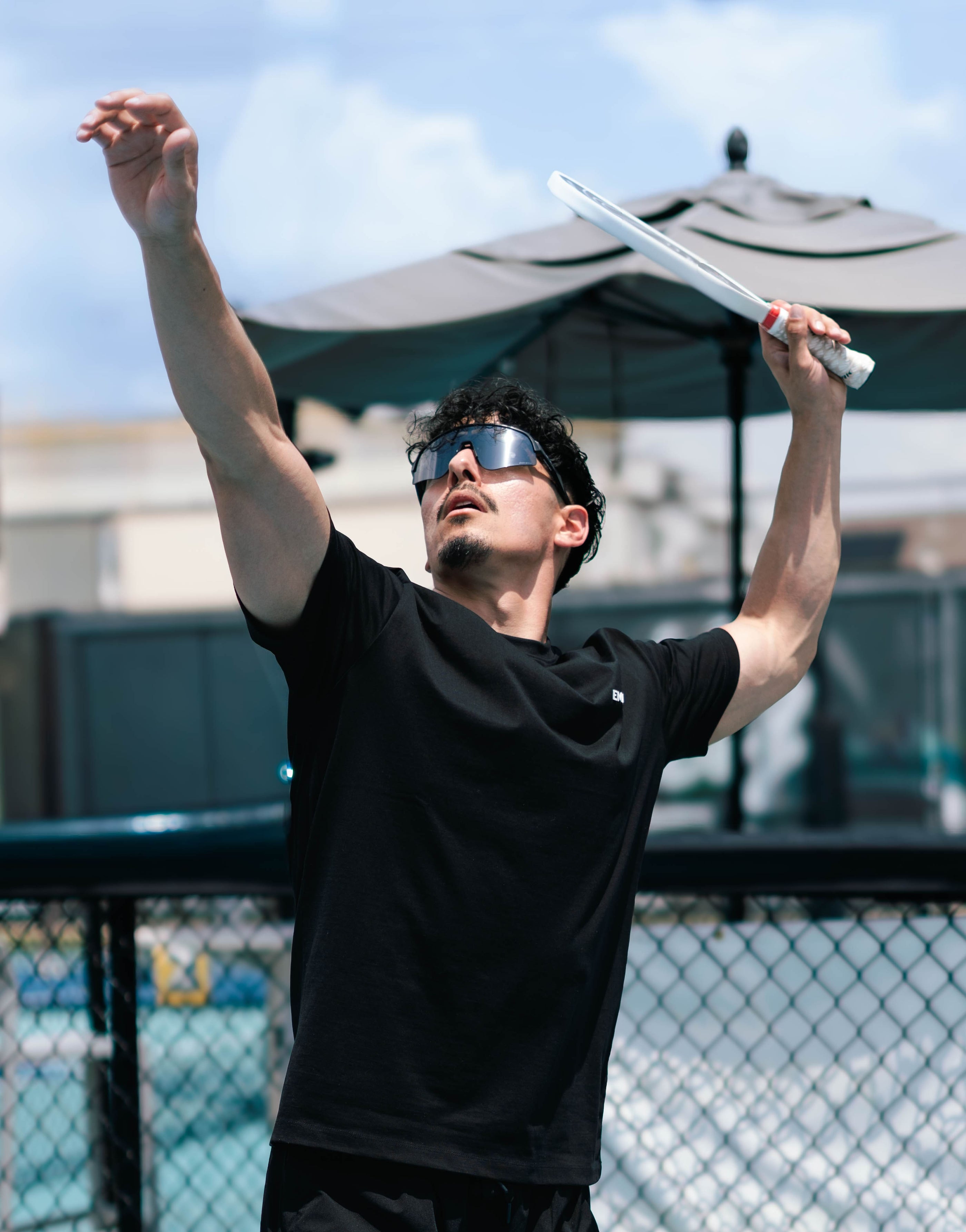 Pickleball player wearing EMANH fitted tee serving
